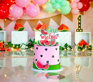 Watermelon themed first birthday cake with One Melon topper, pink frosting, and colorful balloon garland backdrop.