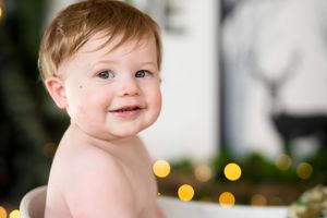 Smiling baby with blue eyes and light brown hair surrounded by bokeh Christmas lights.