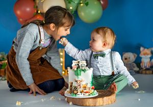 Two young children celebrate a first birthday with an animal-themed cake, sharing a sweet moment together.