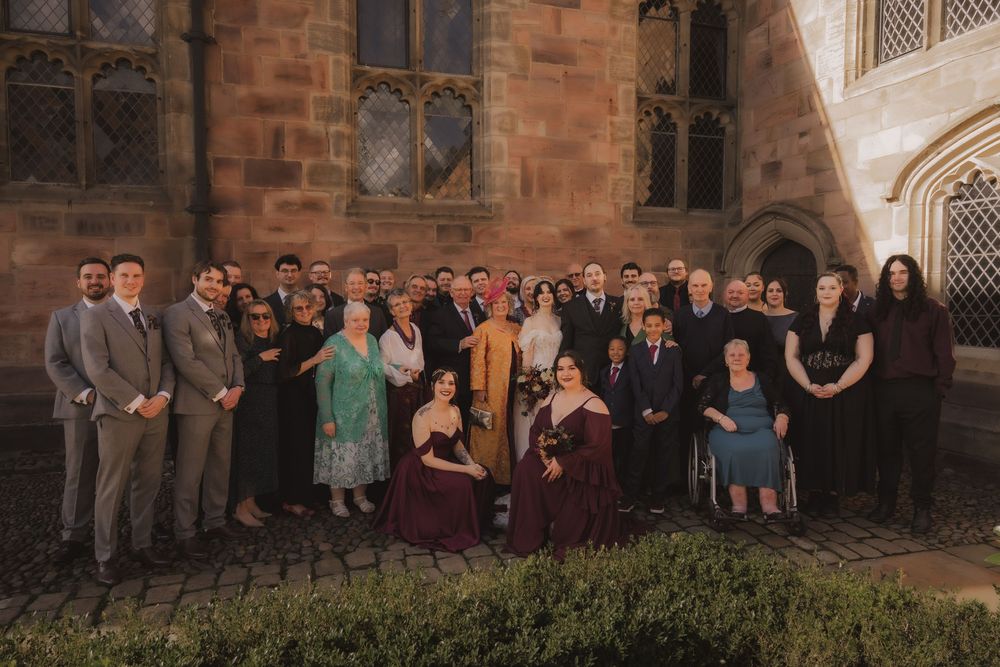 Large wedding party group photo posed outside a historic stone church building at dusk.