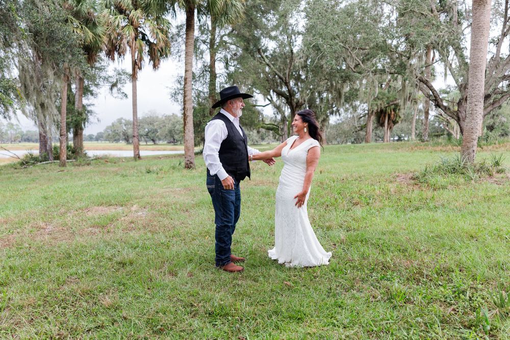 Bride in white gown and groom in cowboy hat share a first look moment outdoors among Spanish moss-draped oak trees.