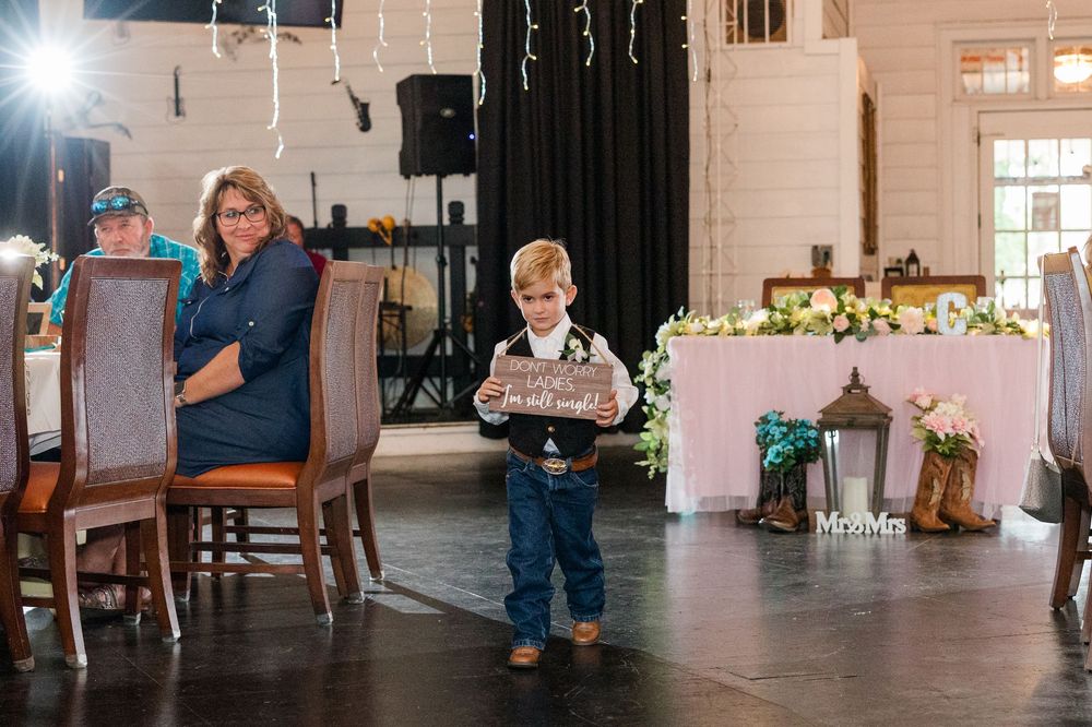 Young ring bearer holds a sign at a rustic wedding reception with floral decorations and Mr. & Mrs. signage.