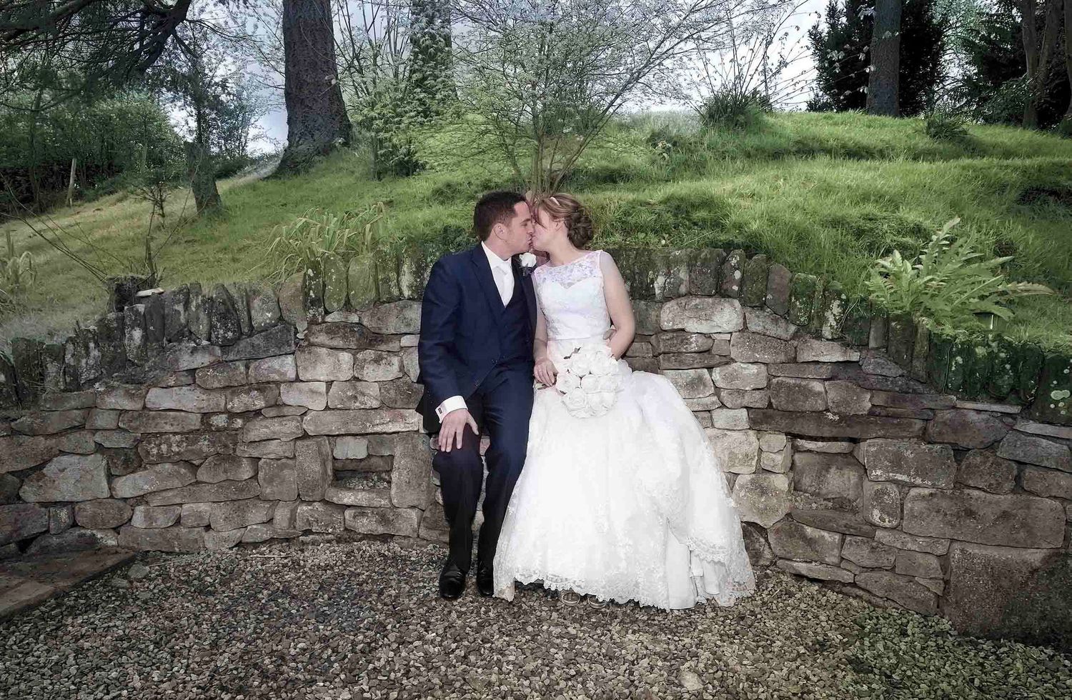Bride and groom sitting close together on a curved stone garden seat at Heather Glen Country House Hotel in Ainstable, Cumbria.