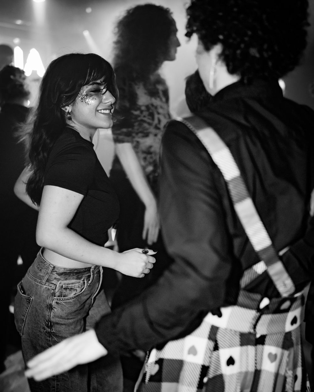 Black and white photo of a smiling woman dancing at a party in jeans and crop top.