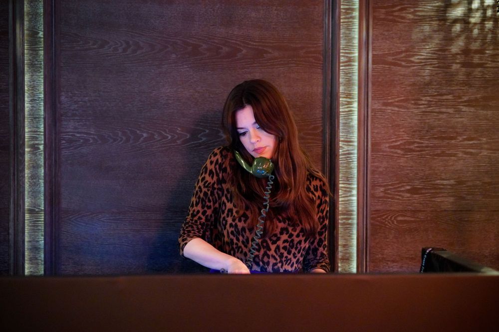 Woman in leopard print top working at a reception desk, focused on paperwork in a dimly lit room.