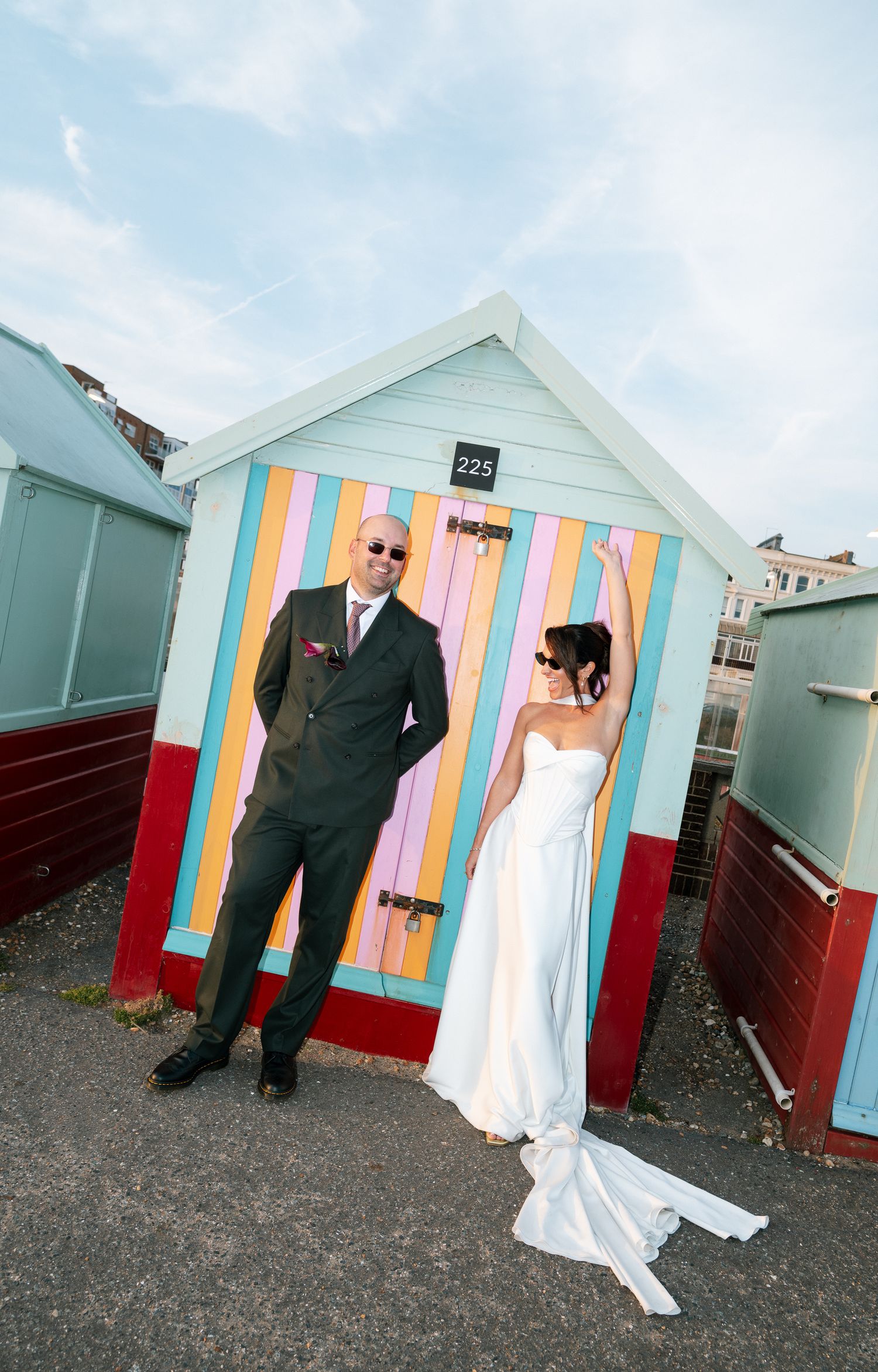 Bride and groom posing in front of colorful beach hut number 225 on their wedding day.