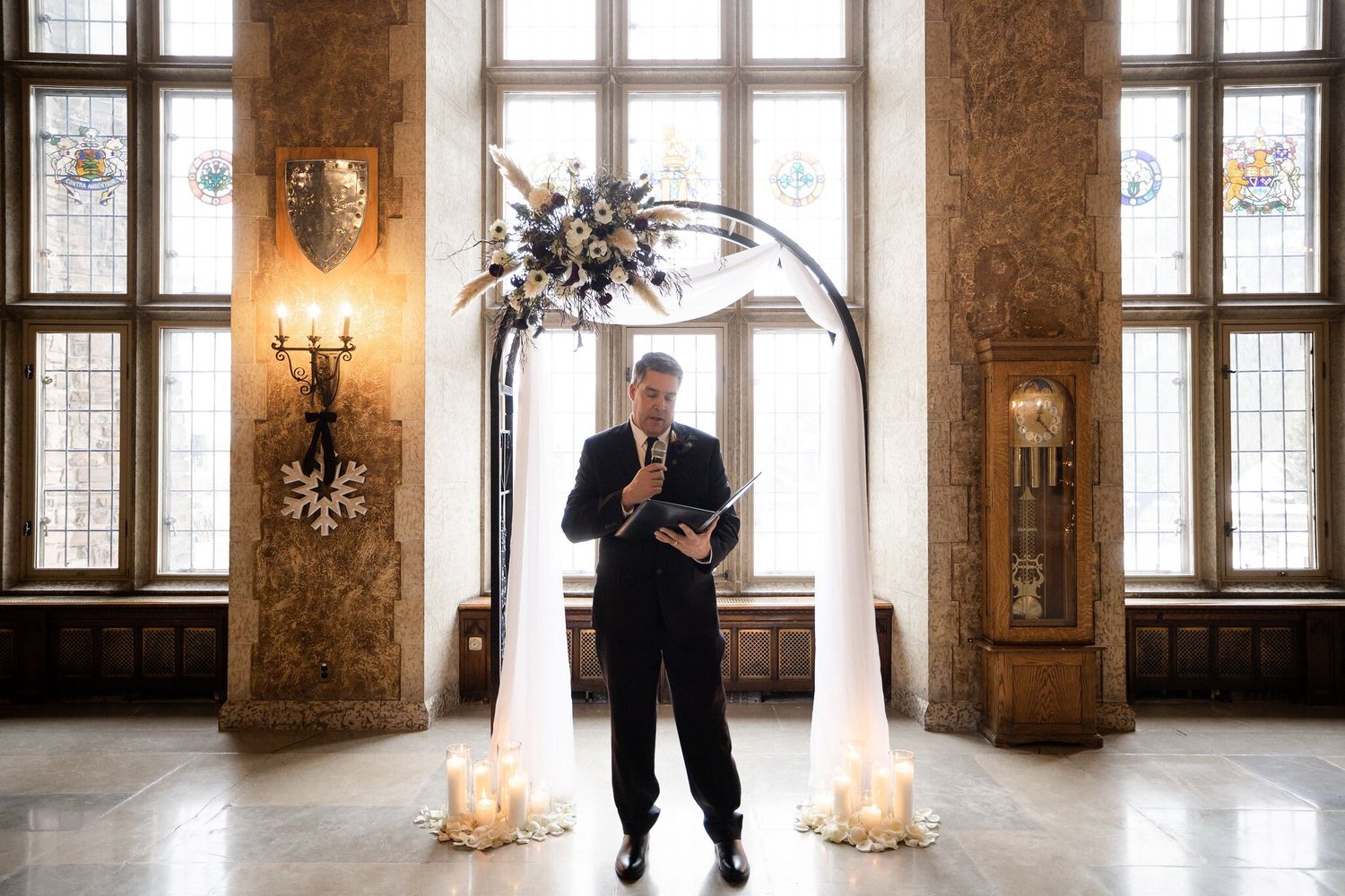 Officiant speaking under a draped floral arch with candles, stained glass and snowflake decor at a Banff wedding ceremony