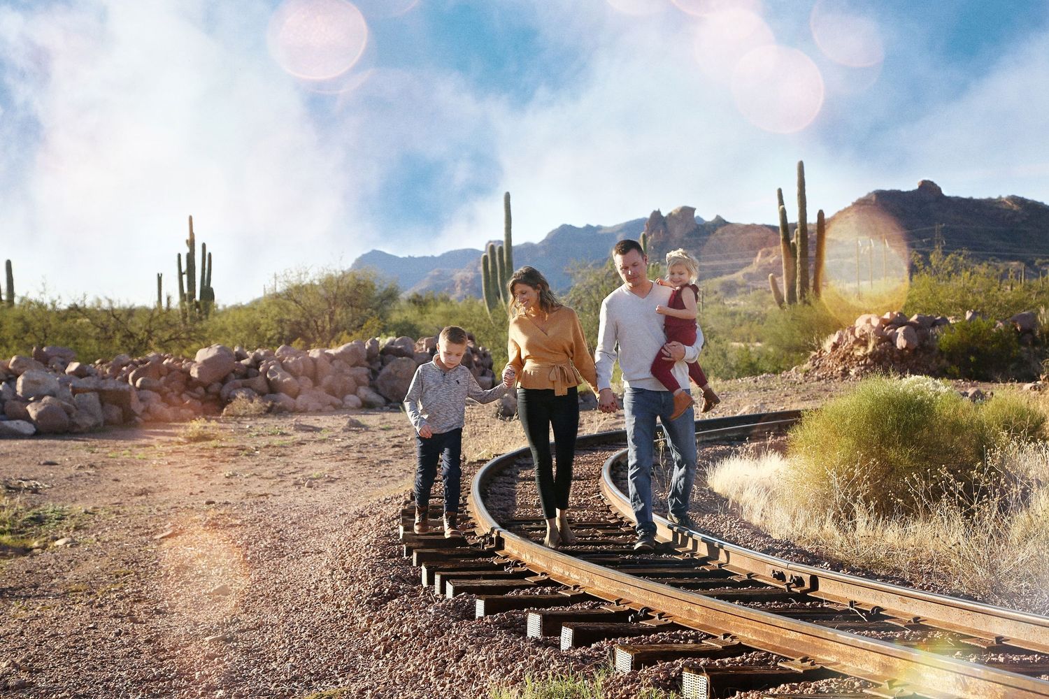 Family of four walking along old railroad tracks in the desert, with saguaro cactus and mountains in the background.