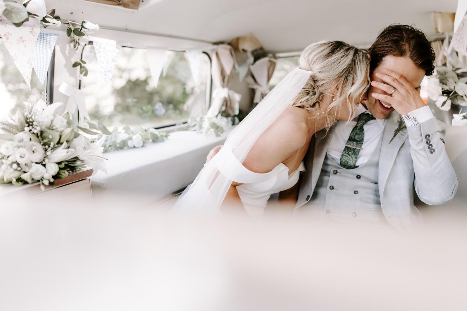 Bride and groom laughing together in the back of their vintage wedding car