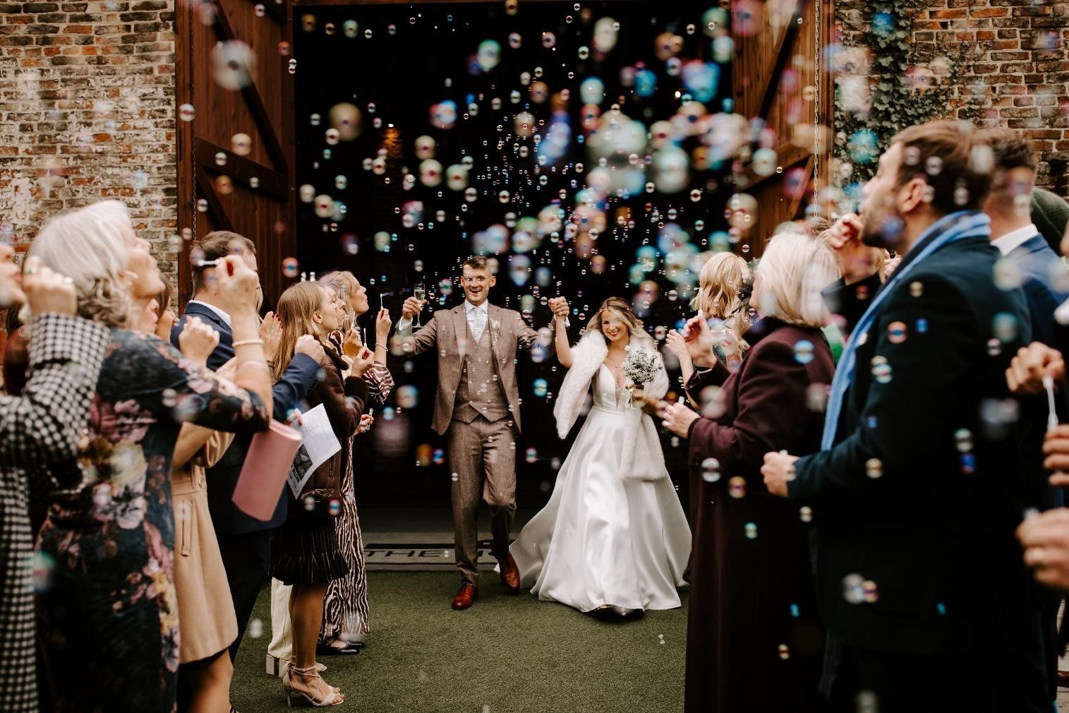 Wedding guests blowing bubbles as the newlyweds walk back down the aisle, photographed by documentary wedding photographer Nick Georgiou