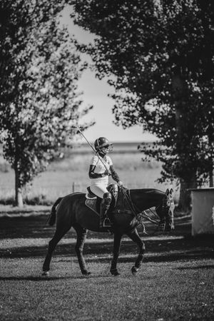 Black and white photo of a polo player riding a dark horse among trees.