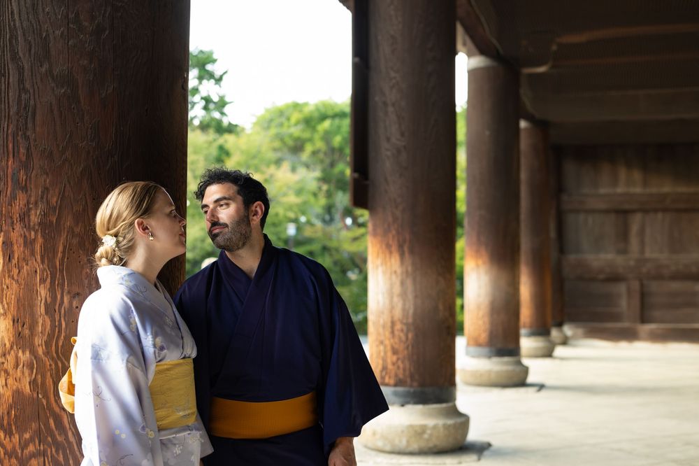 Couple wearing traditional Japanese kimono standing among wooden columns at a Japanese temple.