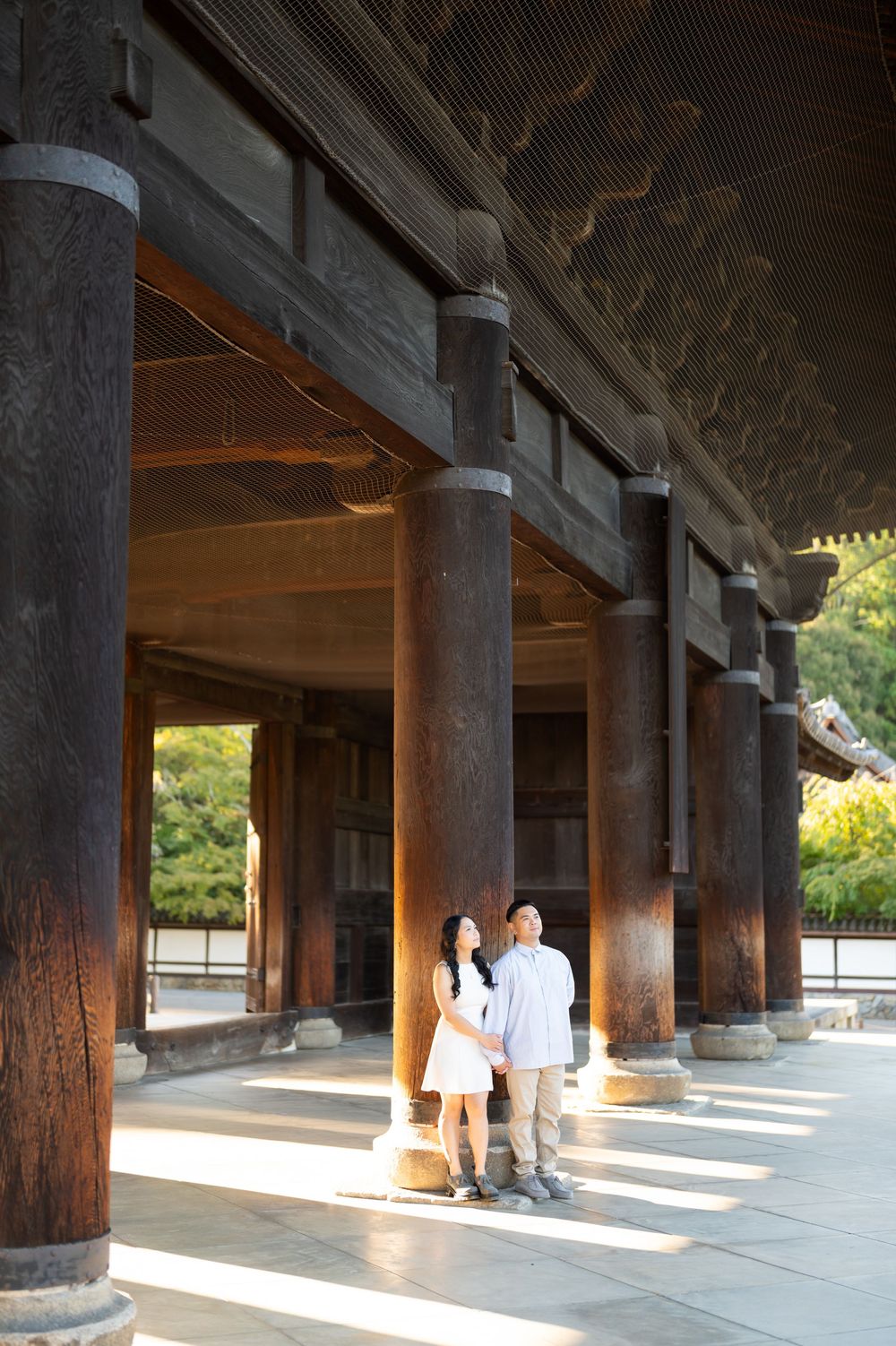Couple holding hands under wooden columns of a traditional Japanese temple, bathed in warm golden sunlight.