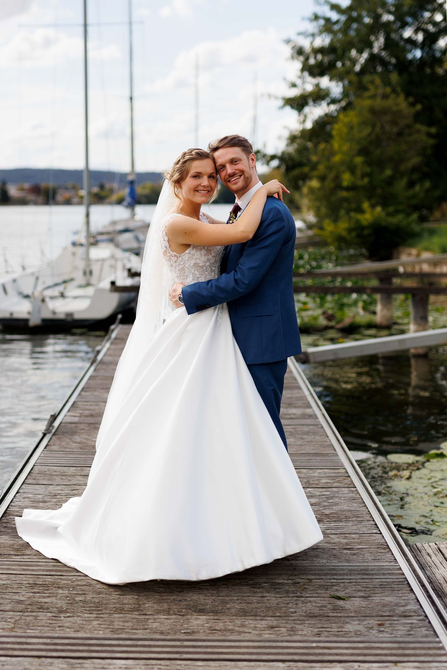 A happy bride and groom embrace on a wooden dock by the water on their wedding day.