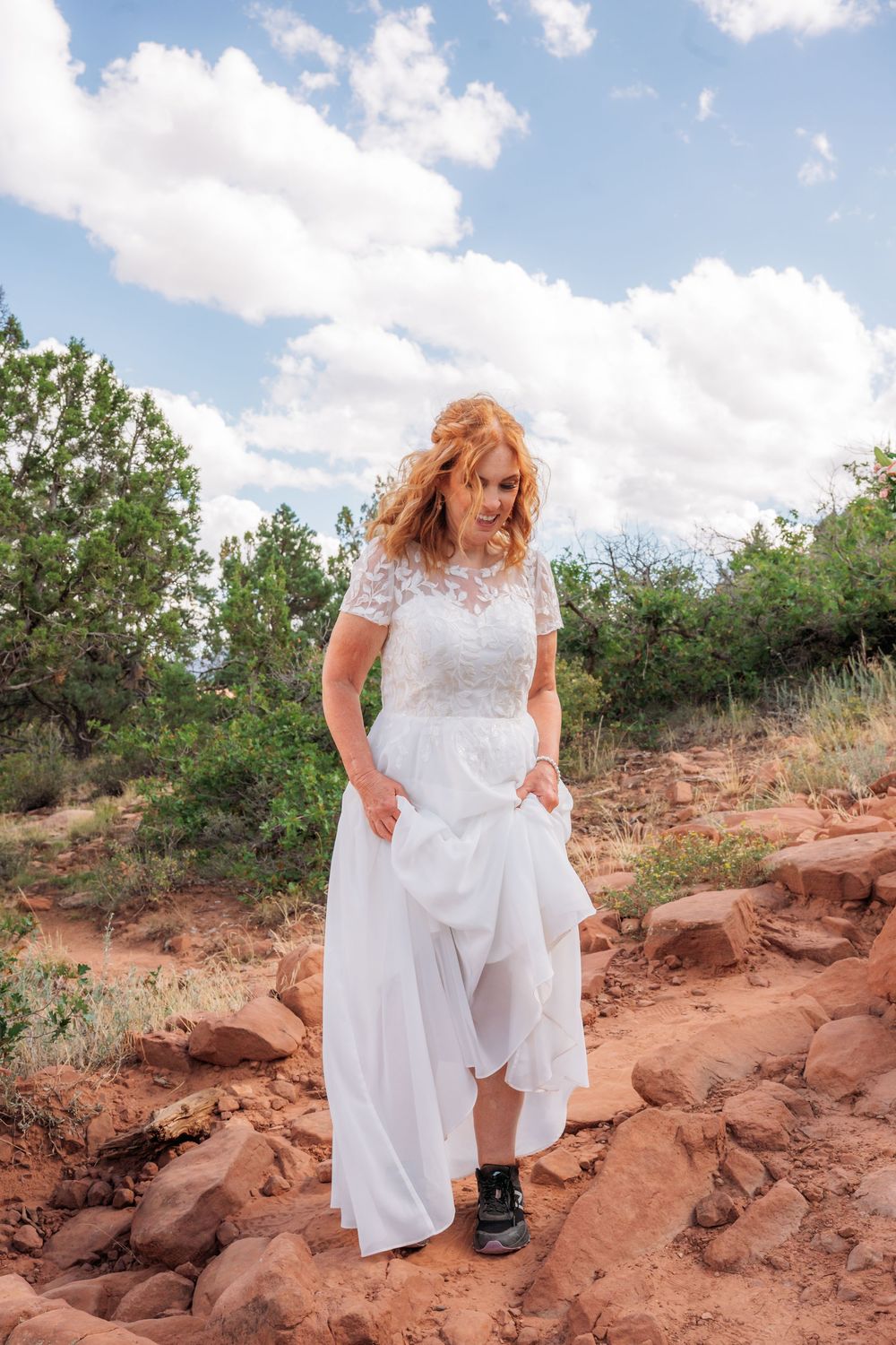 Bride in white lace dress with combat boots walks on red rock trail in Sedona Arizona desert landscape.