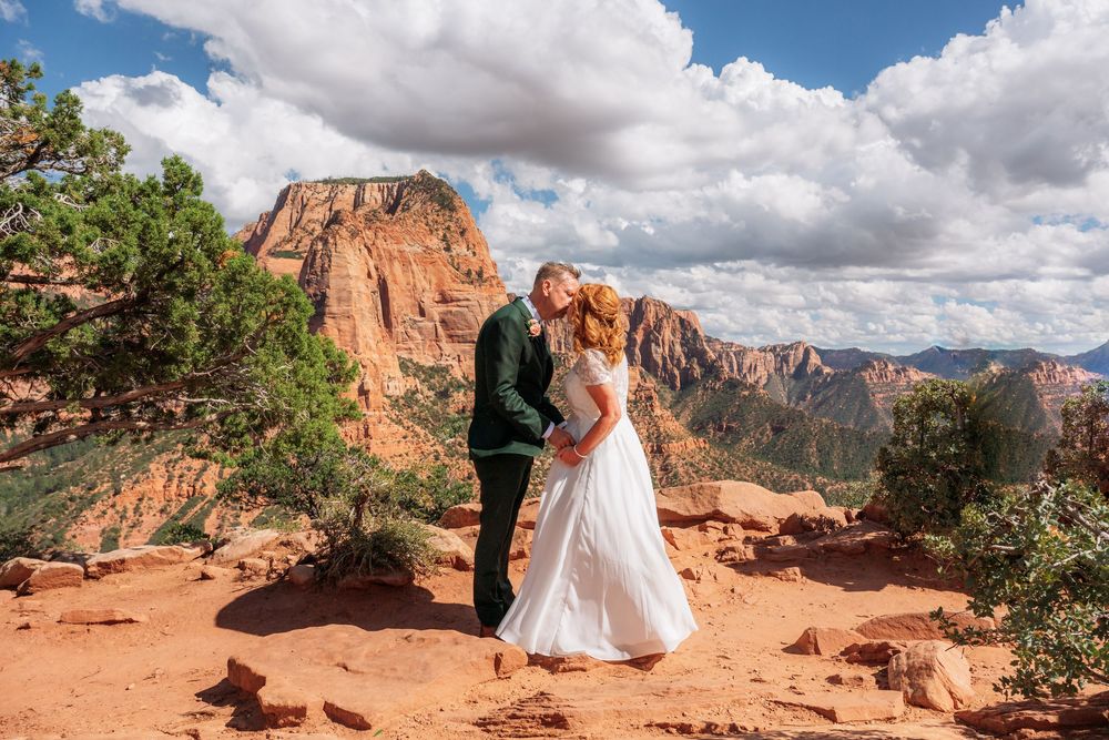 Couple shares romantic kiss on red rock overlook with stunning Sedona Arizona canyon views behind them.