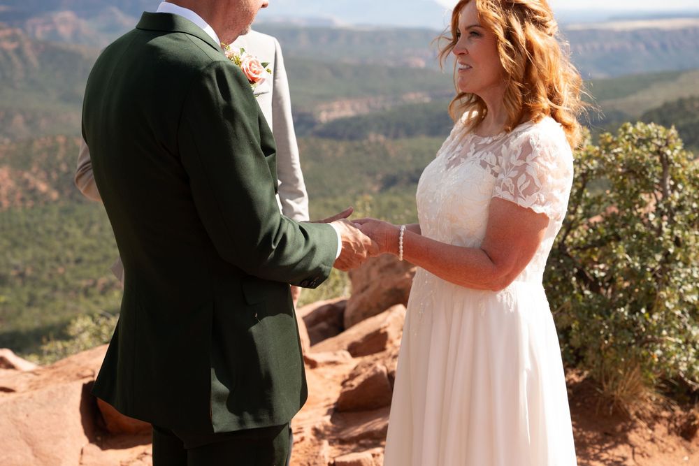Bride and groom exchange wedding vows on red rock cliff with sweeping Arizona canyon valley below.