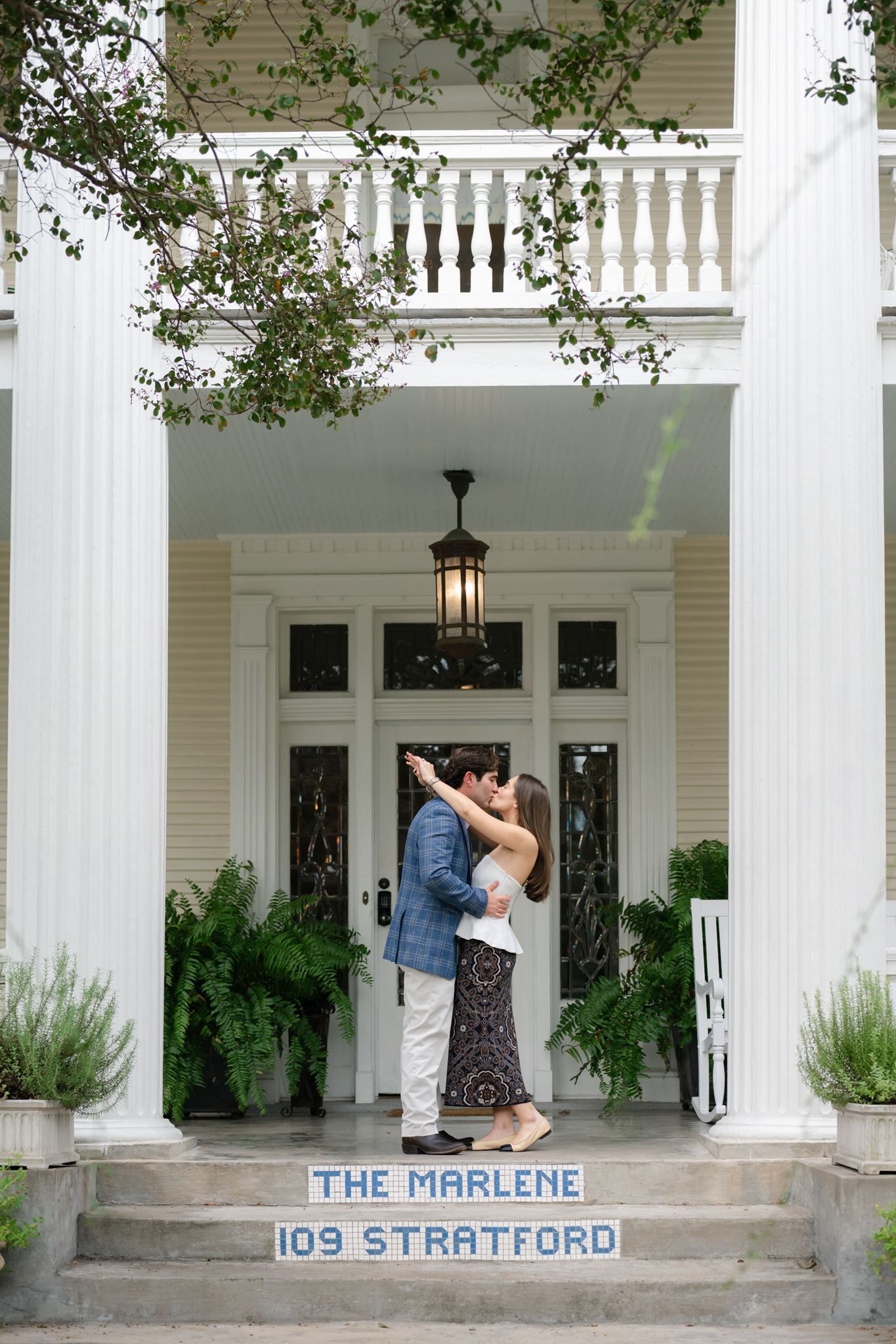 Man and woman sharing a kiss on the front porch of The Marlene hotel in Houston, Texas.
