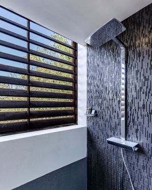 Modern bathroom with large rainfall shower head and textured tile wall next to slatted window.