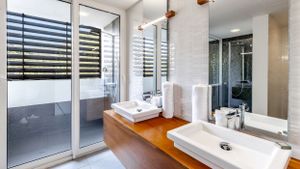Modern bathroom interior with double vanity, wooden countertop and glass shower enclosure.