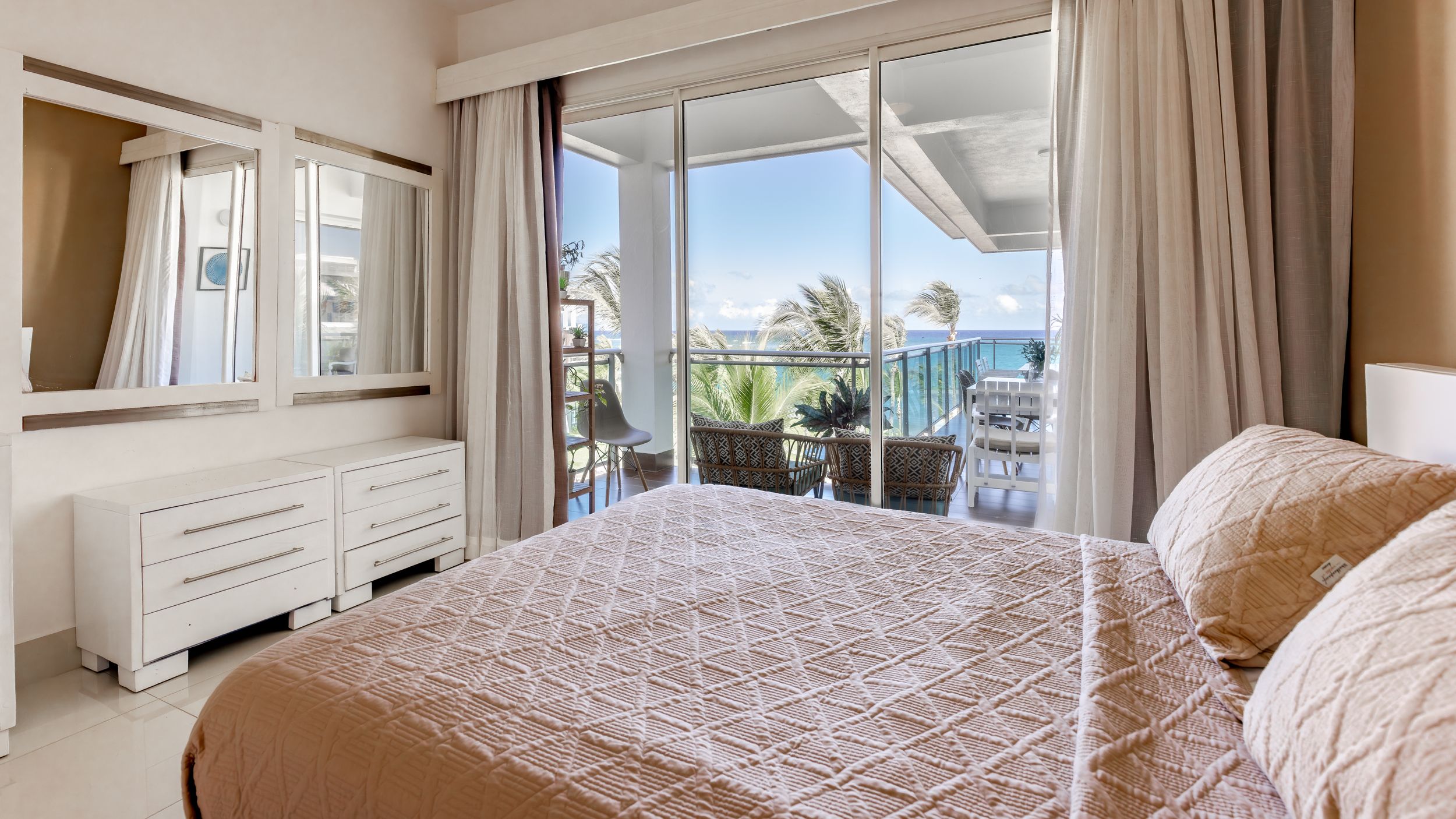 Luxurious bedroom with ocean view through sliding glass doors and elegant white furniture.
