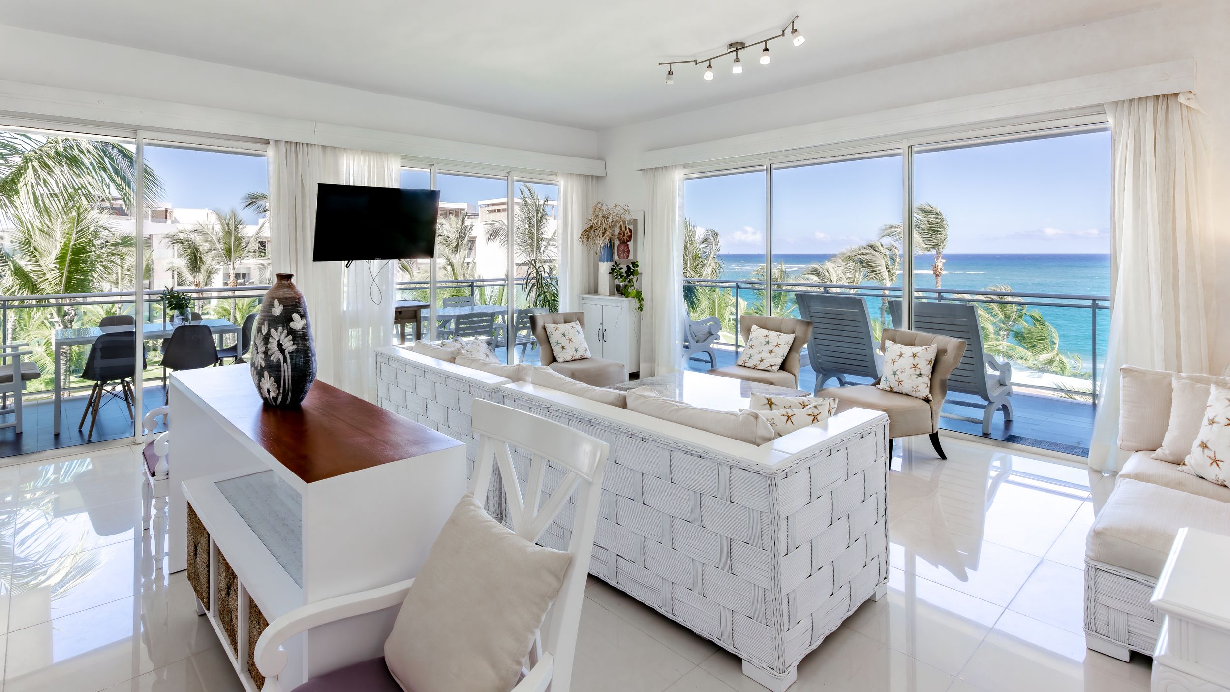 Bright coastal living room with white furniture and stunning ocean views through large windows.