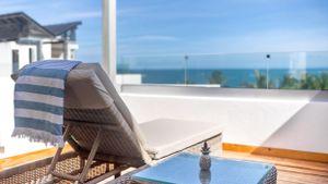 Striped beach lounger on wooden deck overlooking turquoise ocean waters and clear blue sky.