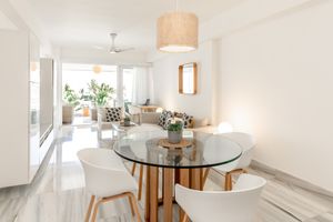 Modern dining area with round glass table, white chairs, and natural light streaming through large windows.