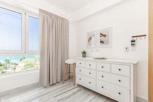 Serene bedroom with ocean view, white dresser, and light gray curtains.