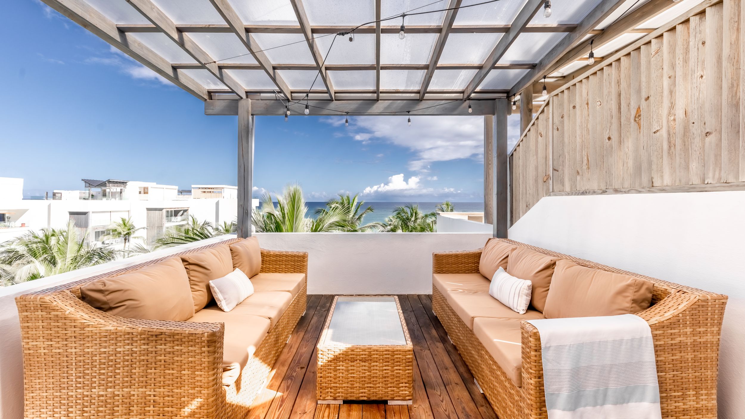 Elegant outdoor seating area with wicker sofas and wooden pergola offering stunning coastal vistas.