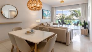 Modern dining and living area with rattan pendant light and ocean view through large windows.