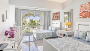 Bright resort room with twin beds, floral decor, and balcony access offering garden views.