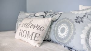 Decorative throw pillows with 'Welcome Home' text and geometric patterns in soft gray tones.