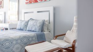 Coastal bedroom with blue patterned bedding and white rocking chair next to small side table.