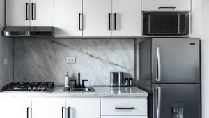 Modern white kitchen with marble backsplash, stainless steel appliances, and contemporary cabinet hardware.