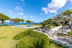 Luxurious oceanfront property with infinity pool, manicured lawn, and tropical landscaping under blue skies.