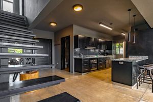 Contemporary black and wood kitchen with floating stairs and open floor plan design.