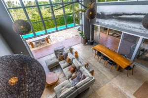 Double-height living area with large windows, modern furniture, and long dining table viewed from above.