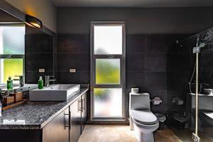 Sleek modern bathroom with dark tile walls, granite countertops, and frosted glass windows.