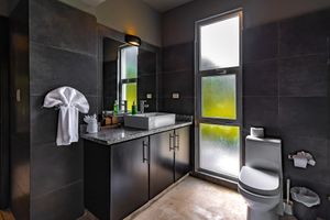 Modern bathroom featuring dark tile walls, floating vanity, and frosted windows providing natural light.