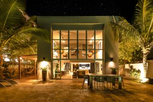 Modern beach house with glass walls illuminated at night among palm trees.