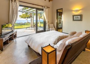 Modern bedroom with sliding glass doors showcasing ocean views, white bedding, and contemporary furniture.