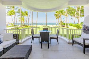 Covered oceanfront patio with comfortable seating arrangement and palm tree lined beach view.