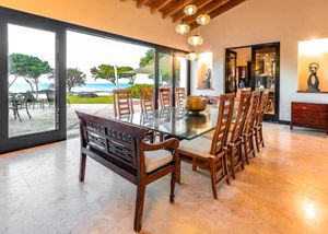 Formal dining room with high-backed chairs offering panoramic ocean views through sliding glass doors.