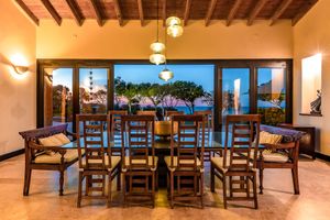 Elegant dining room with wooden beams and ocean views through large windows at sunset.