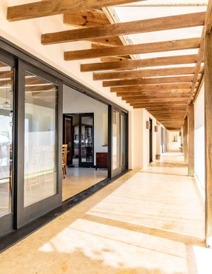 Long covered walkway with exposed wooden beams and glass sliding doors leading to interior spaces.
