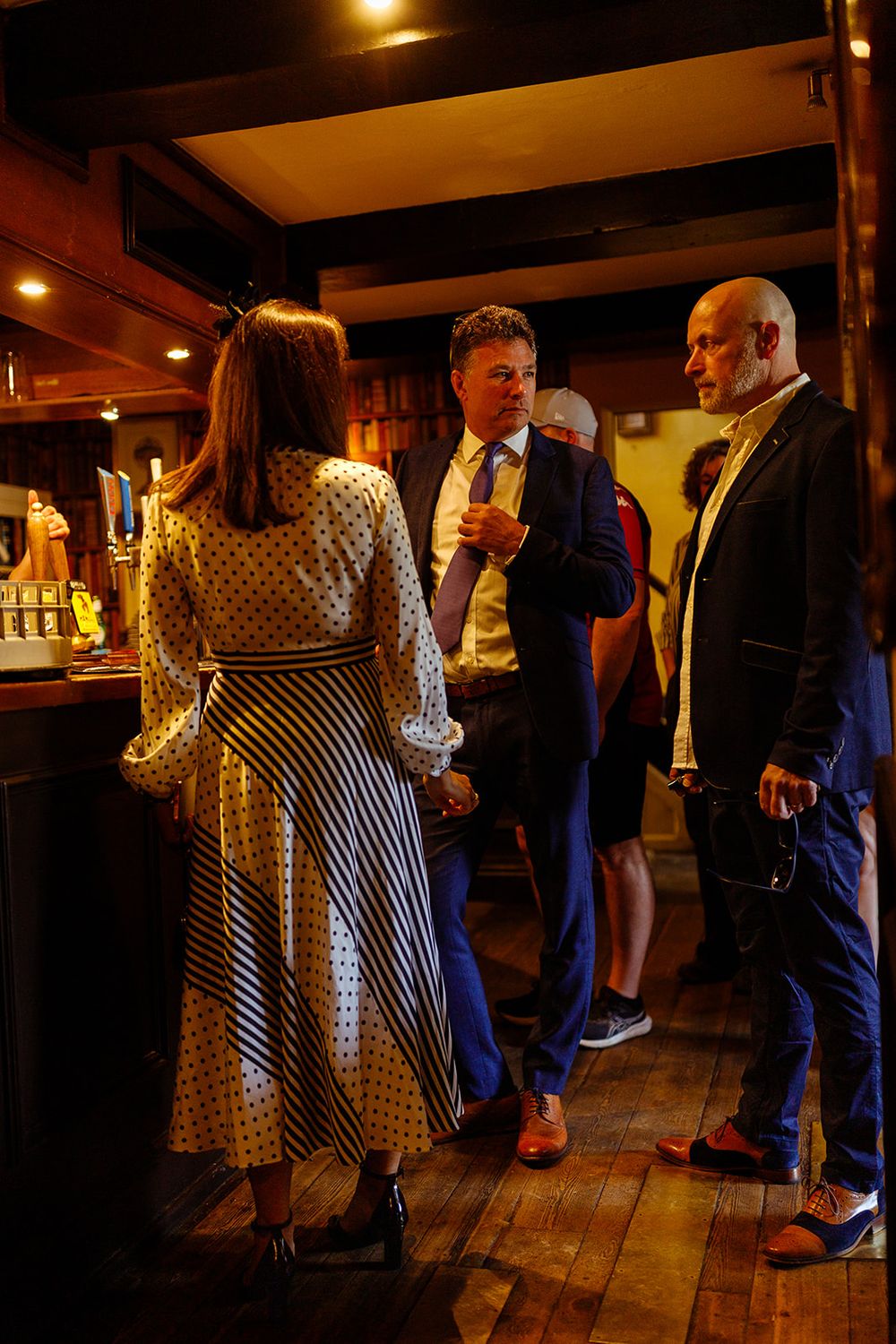 Elegantly dressed guests socializing at a warmly lit bar venue during a formal evening event.