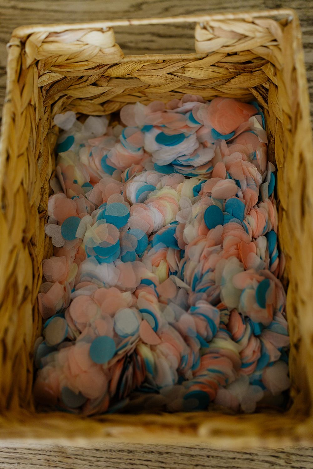 Wicker basket filled with colorful pink, blue, and white paper confetti circles for a celebration or party.