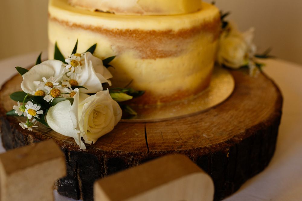 Rustic naked wedding cake on wooden log slice adorned with white roses and daisies.