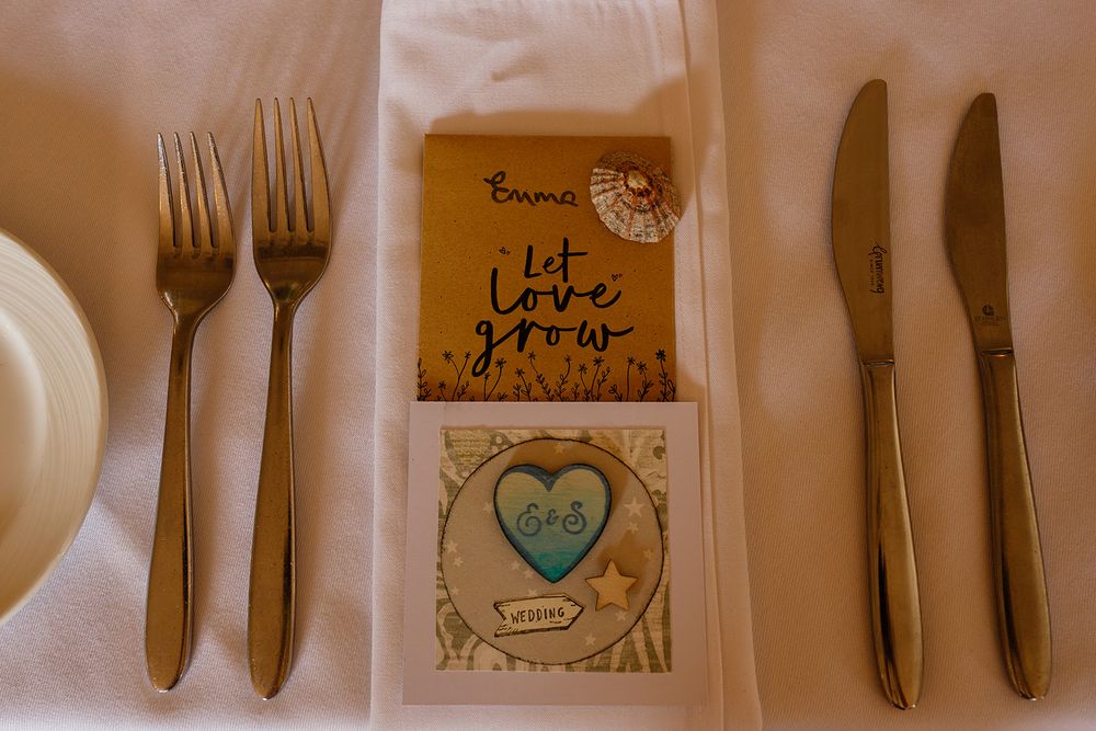 Wedding place setting with two forks, knives, napkin, and seed packet favor reading let love grow on white tablecloth.
